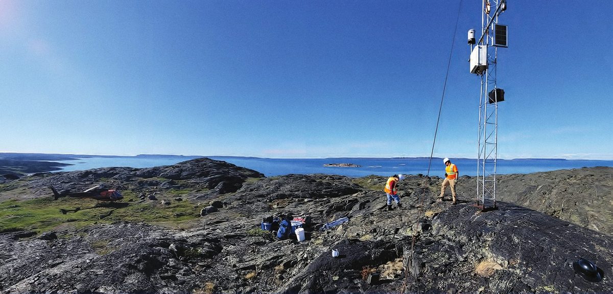 Workers and a helicopter on the rocky coastline near Grays Bay, Nunavut, during survey work.